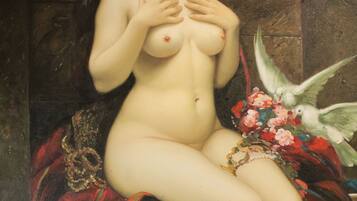 A classical painting of a nude figure seated on a red and green draped chair, surrounded by flowers and birds.