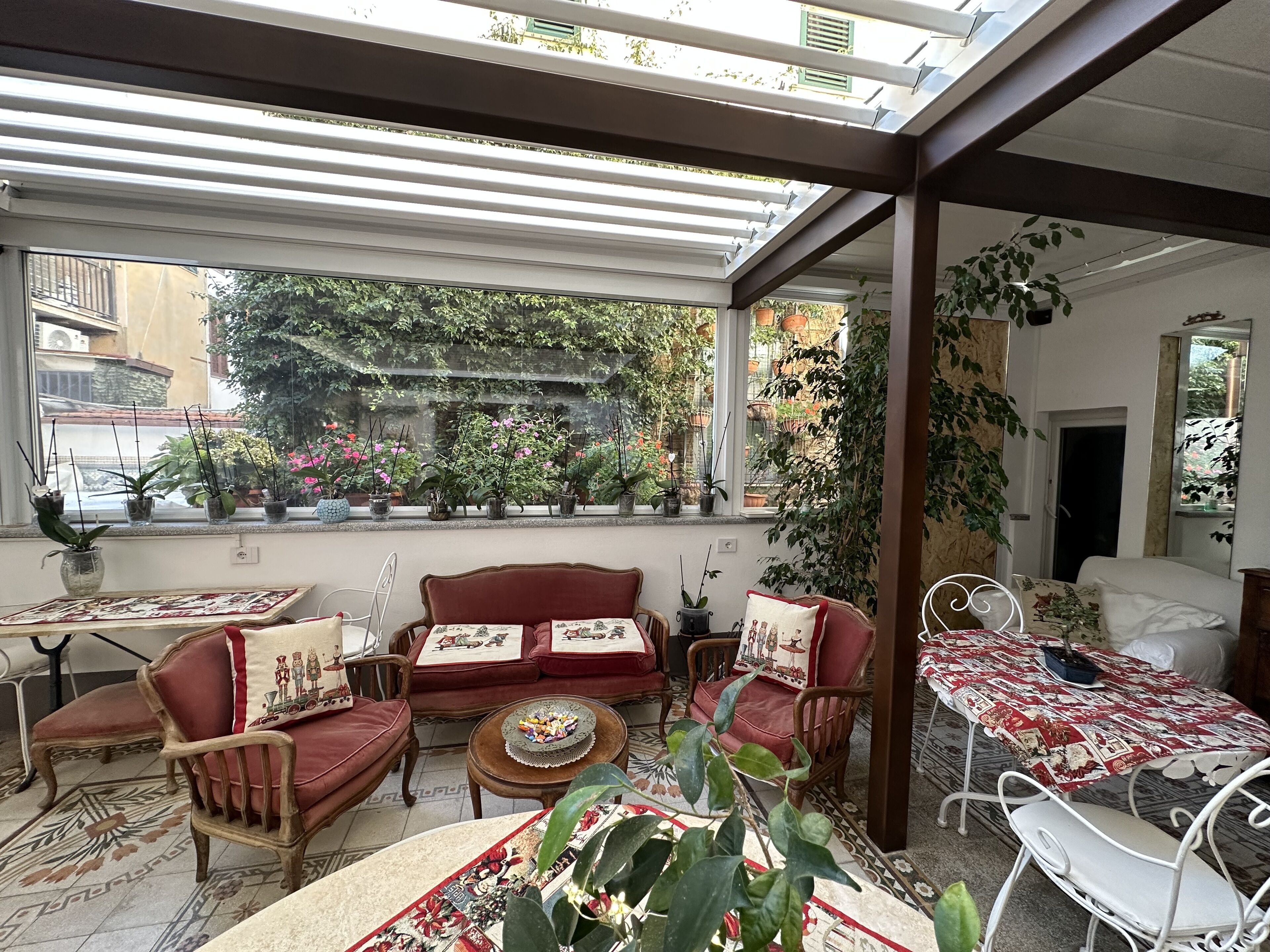 A sunlit room with a red sofa, a white chair, and a table with a patterned tablecloth.