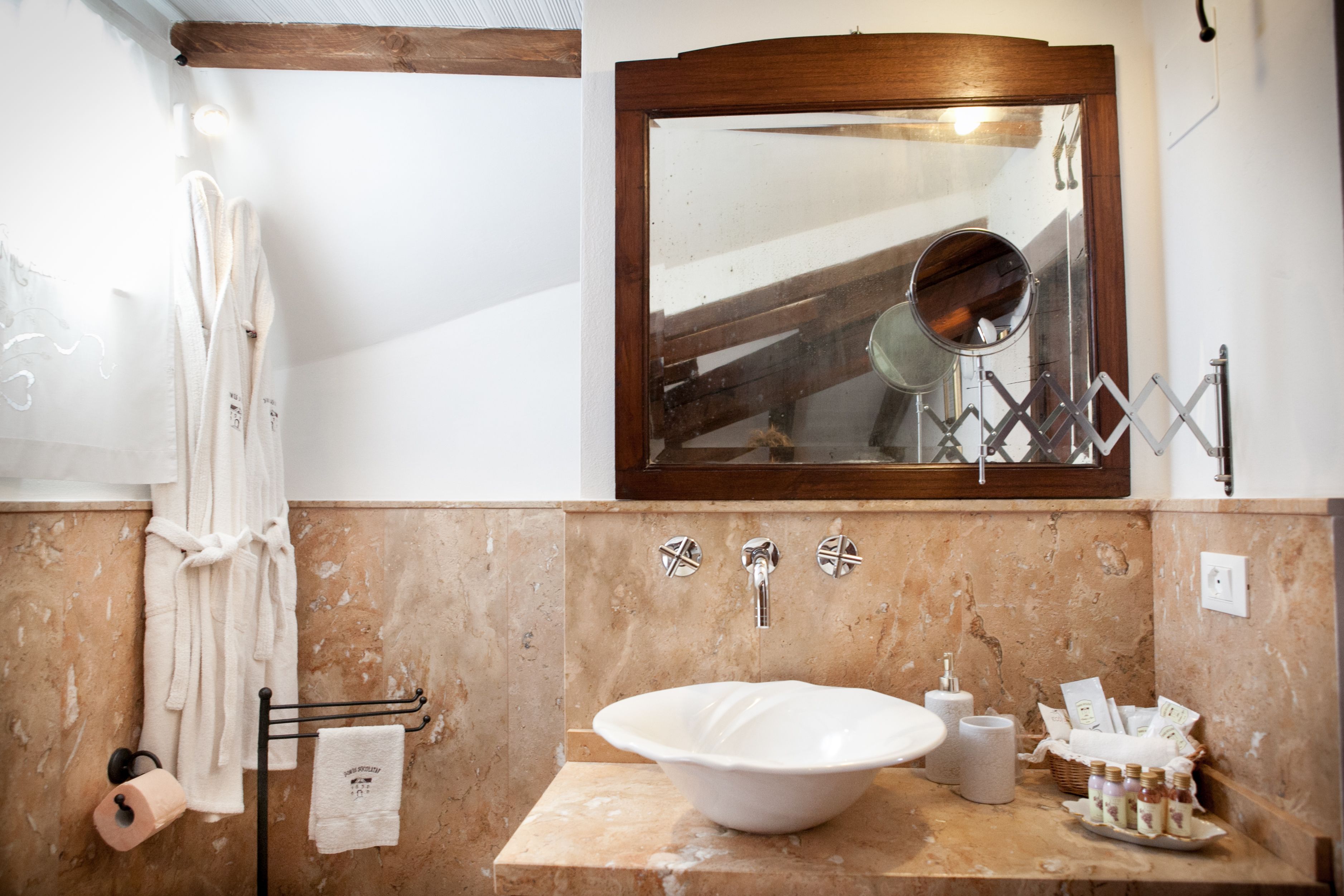 Ein Badezimmer mit Marmorwand, einem spiegelnden Holzbettrahmen, einem Waschbecken und Handtüchern, die an einem Wäscheständer hängen.