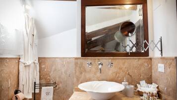 Ein Badezimmer mit Marmorwand, einem spiegelnden Holzbettrahmen, einem Waschbecken und Handtüchern, die an einem Wäscheständer hängen.