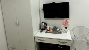 A small, clean room with a white desk, a flat-screen TV, a wardrobe, and a trash bin. - Napoli Relais (Naples)