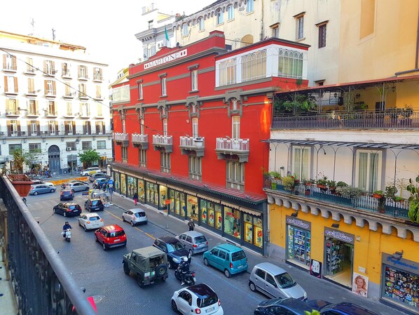 A busy street with a red building labeled "MARTONE" and various shops. - A ddurmì (Naples)