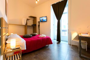 A hotel room with a bed, a desk, a chair, a TV, and a window with curtains. - A ddurmì (Naples)