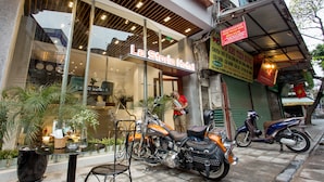 Een hotel ingang met een neonreclame, terras en geparkeerde motorfietsen.