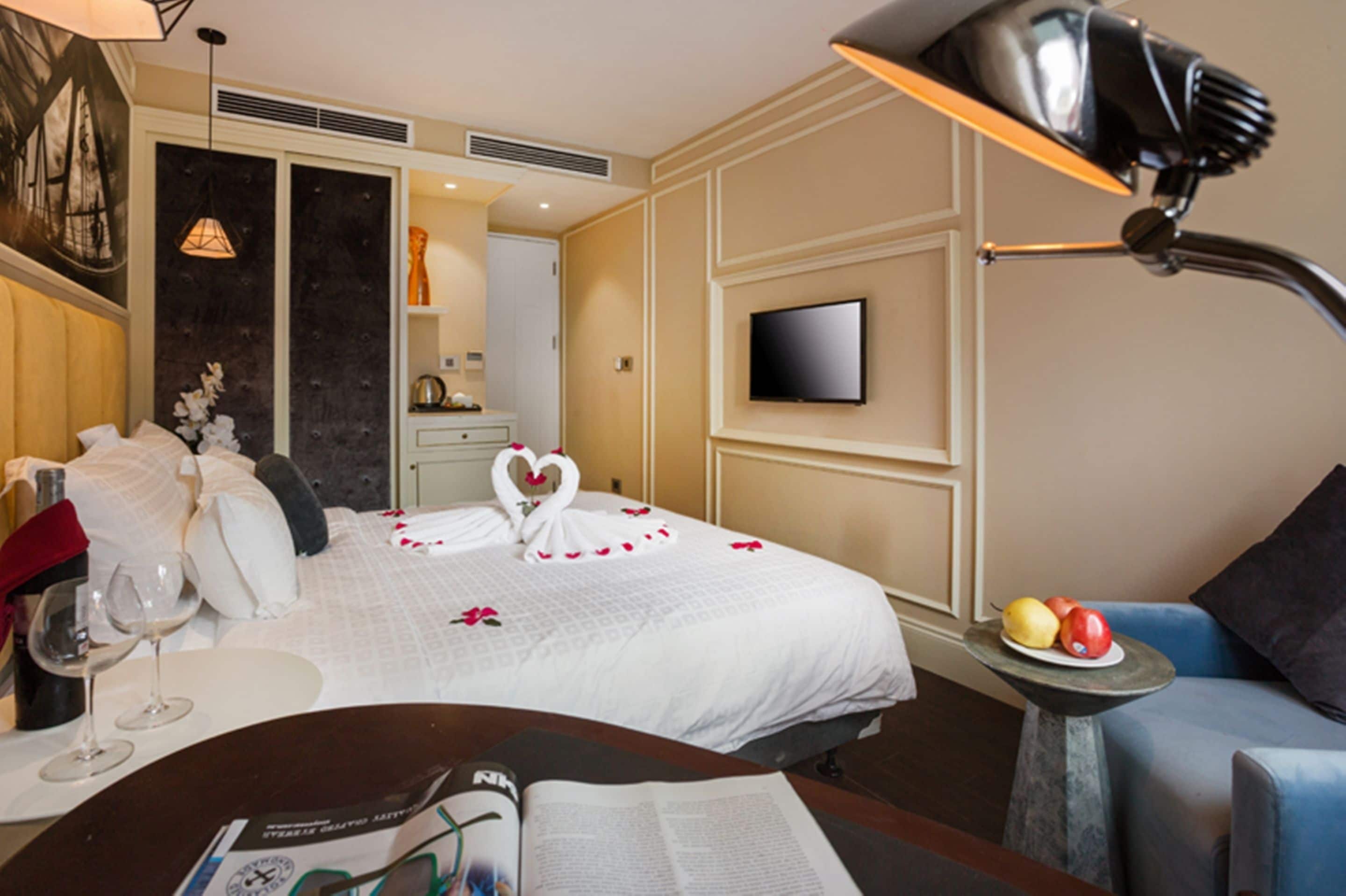 Una habitación de hotel con una cama, televisión, escritorio con una revista y una mesita con fruta.