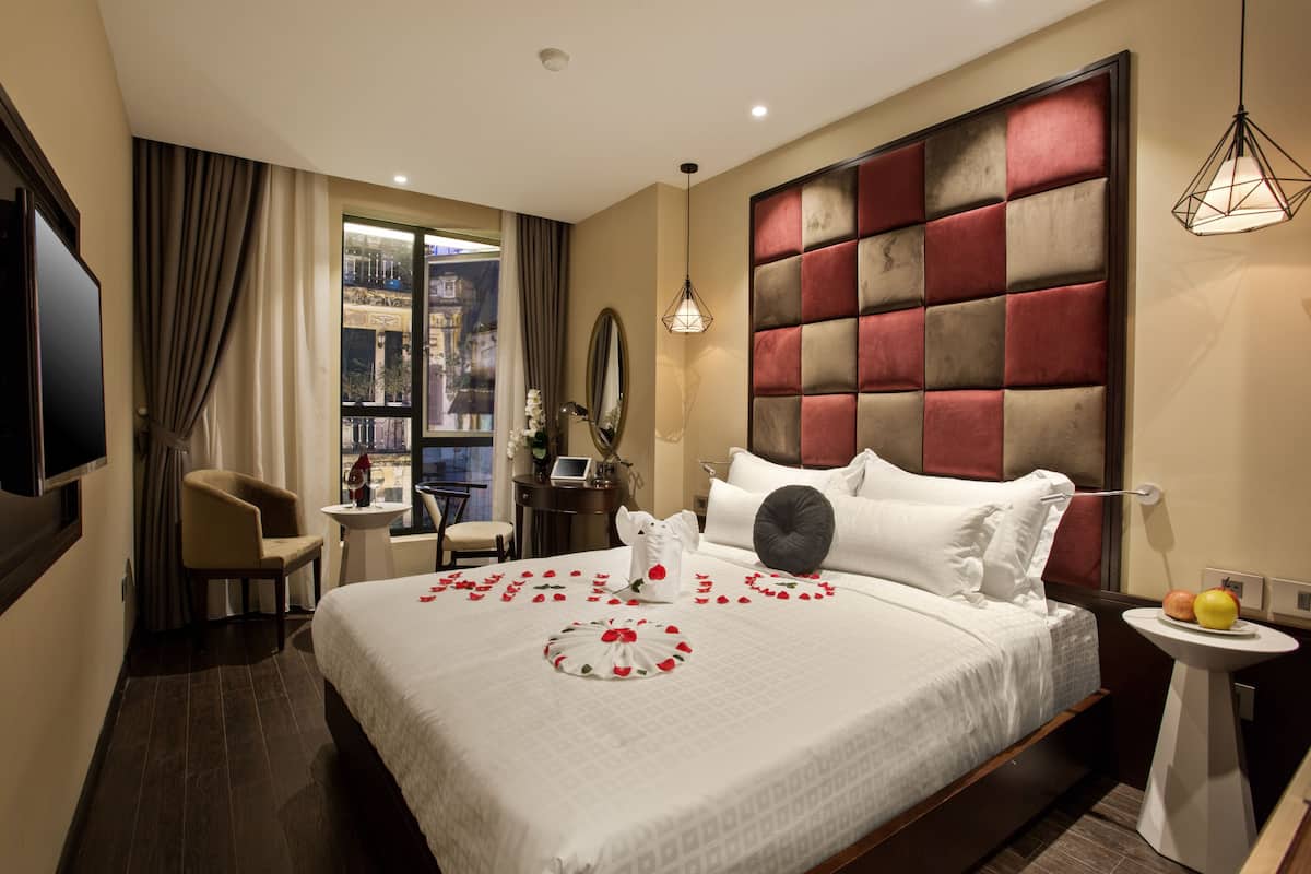 A hotel room with a large bed, a desk, a chair, a TV, and a window with curtains.