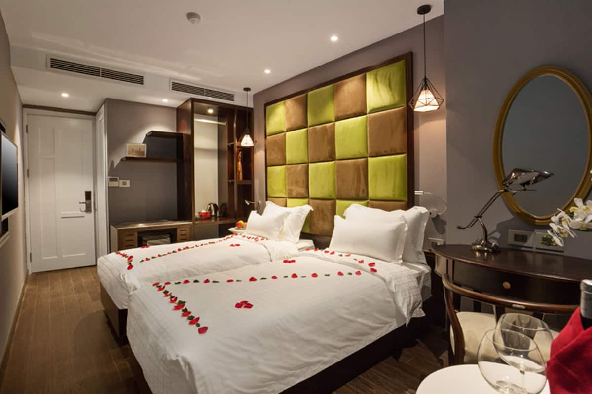 A hotel room with two beds, a large mirror, a vanity with a mirror, and a small table with a glass.
