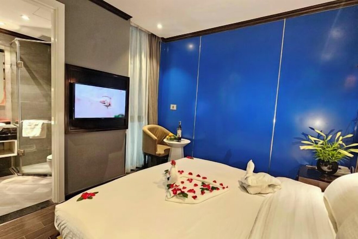 A hotel room with a bed, a TV mounted on the wall, a shower area, and a blue accent wall.
