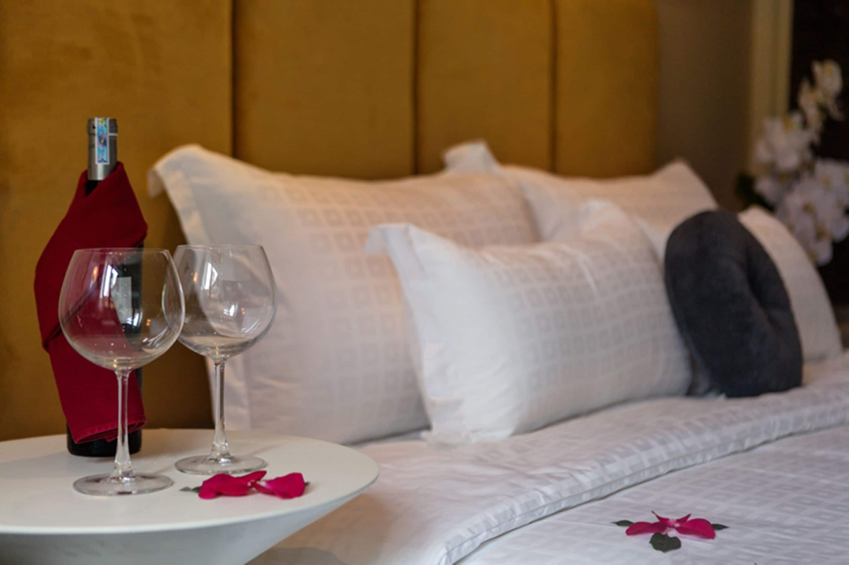 A neatly made bed with white bedding and a red napkin on a small table beside it.