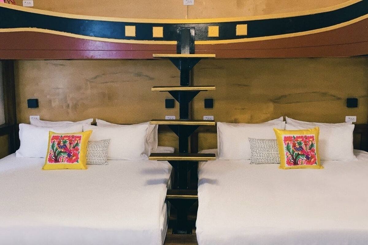 A double bed with white linens and floral pillows, a wooden headboard, and a unique ceiling design.