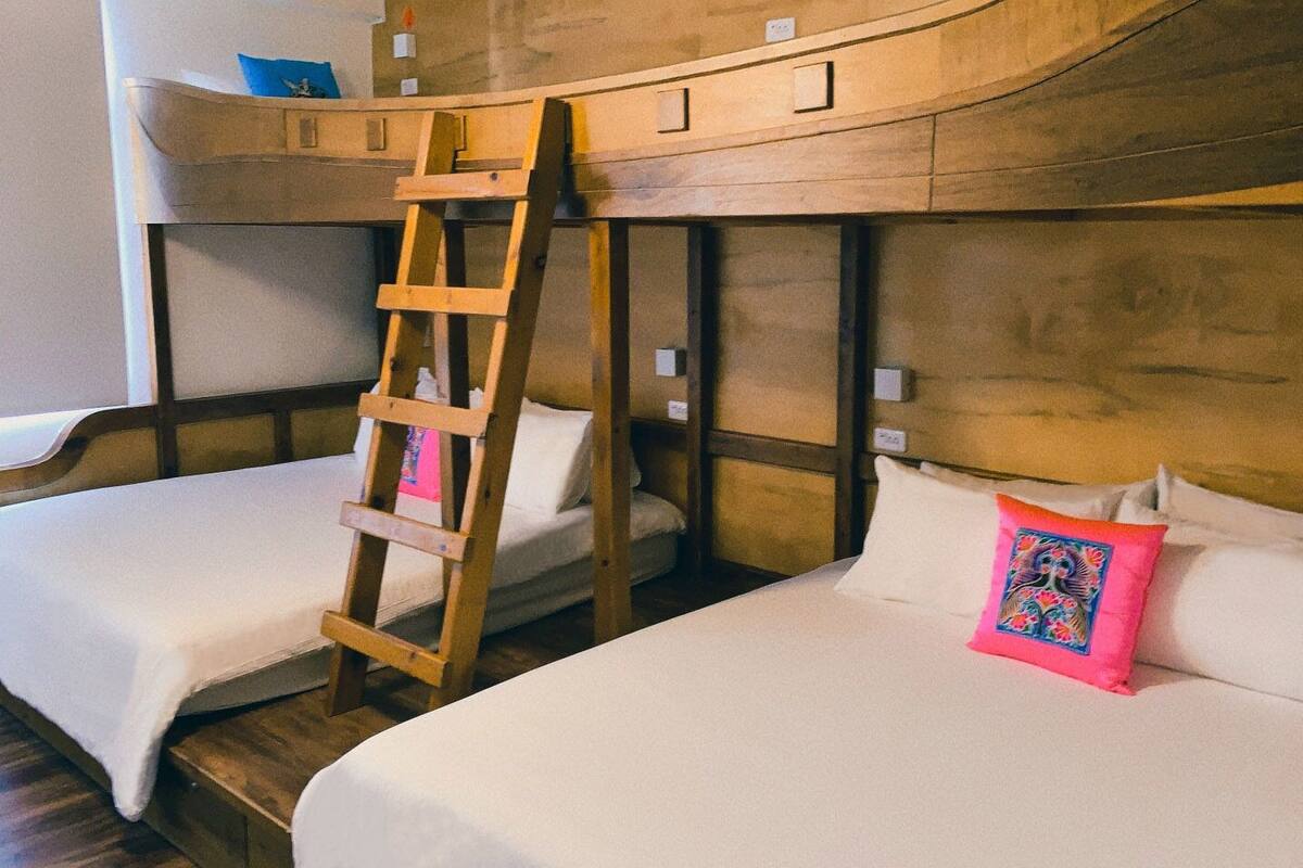 A bunk bed room with a wooden ladder, white bedding, and a colorful pillow.