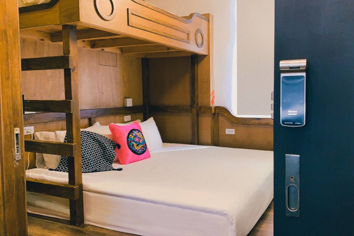 A bunk bed with a wooden headboard, a white mattress, and a pink pillow. There is a door with a silver handle and a keyhole.