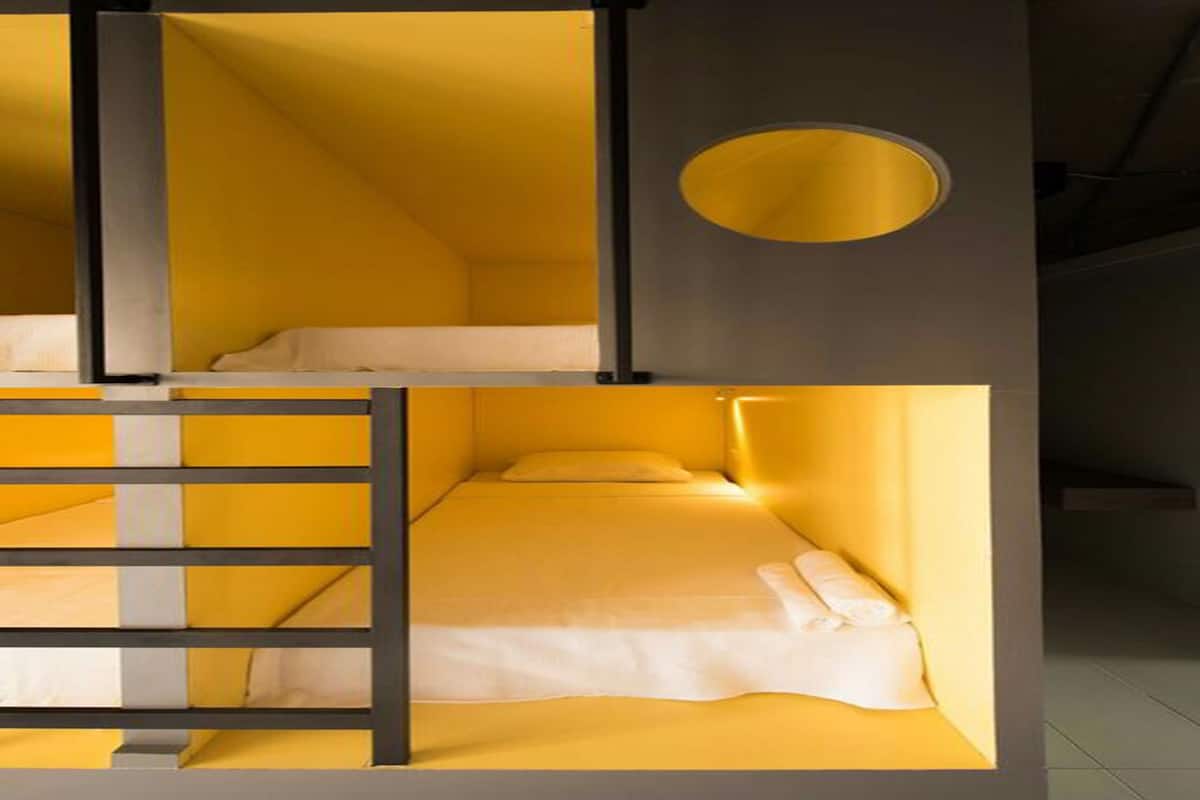 Ett hotellrum med en inredning i gula nyanser, en våningssäng och ett runt fönster.