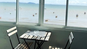 A view from a room with a large window overlooking a calm sea with several boats. There is a wooden table and two chairs in the foreground. - Betta Hostel (Chonburi)
