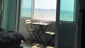A room with a bed, a small table with chairs, and a view of the beach through large windows. - Betta Hostel (Chonburi)