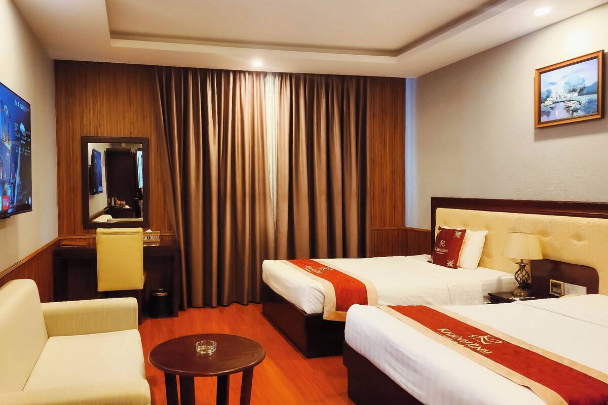 A hotel room with two beds, a desk, a chair, a TV, and a painting on the wall.
