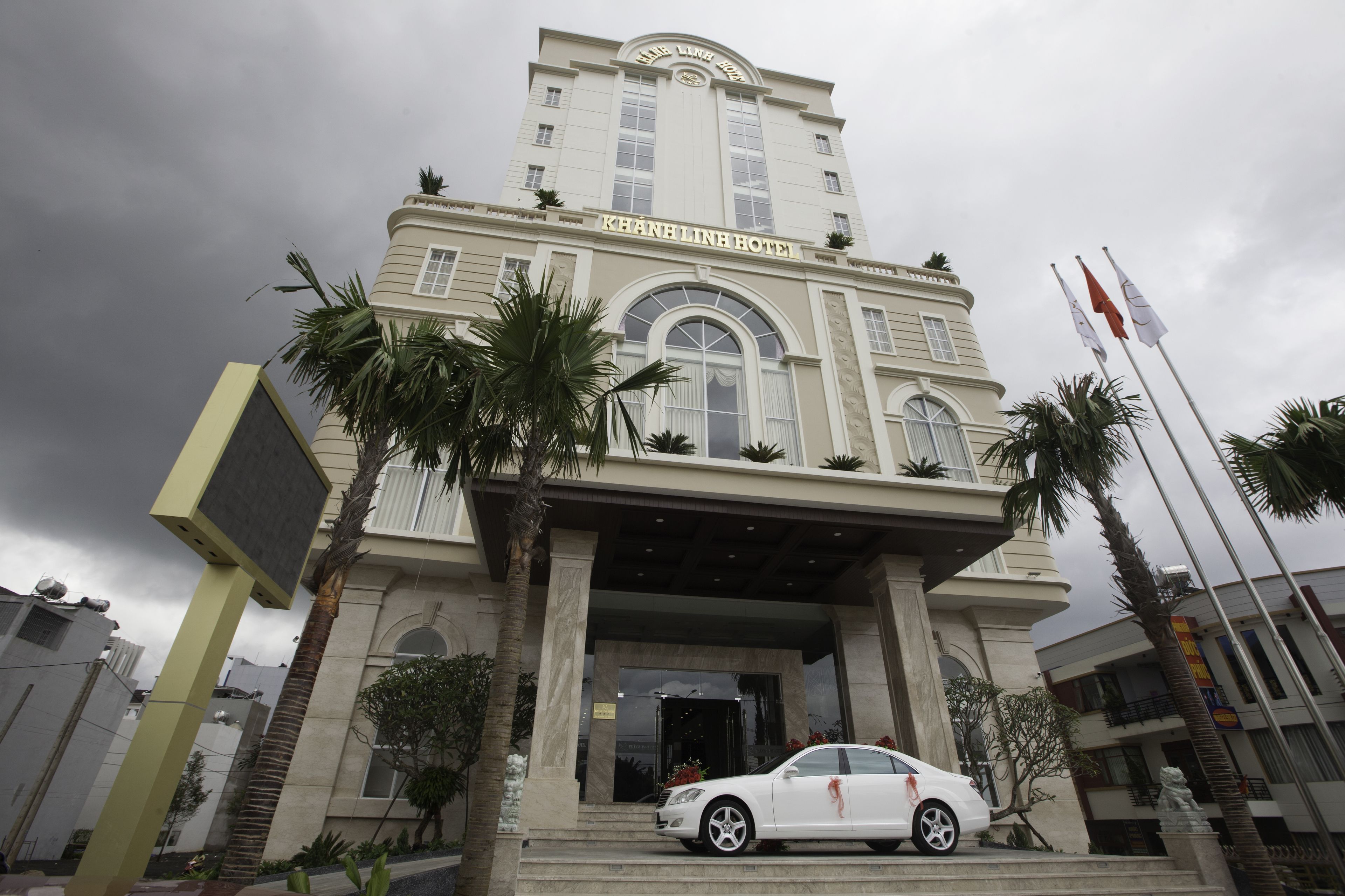 A hotel with a grand entrance, palm trees, and a white car parked in front.