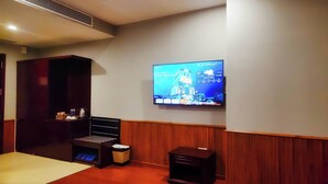 A hotel room with a flat-screen TV mounted on the wall displaying a welcome message, a wooden cabinet, a trash bin, and a small table with a lamp. - Khánh Linh Hotel (Pleiku)