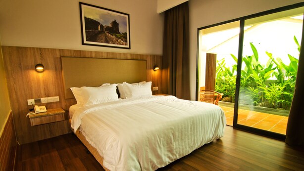 A hotel room with a large bed, wooden headboard, bedside lamps, a telephone, and a view of greenery through a glass door. - MyDream Homestay (Ipoh)