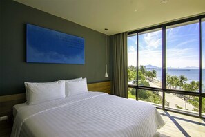 A hotel room with a large bed, a view of the beach, and a blue wall with text. - Kalm Bangsaen Hotel (Chonburi)
