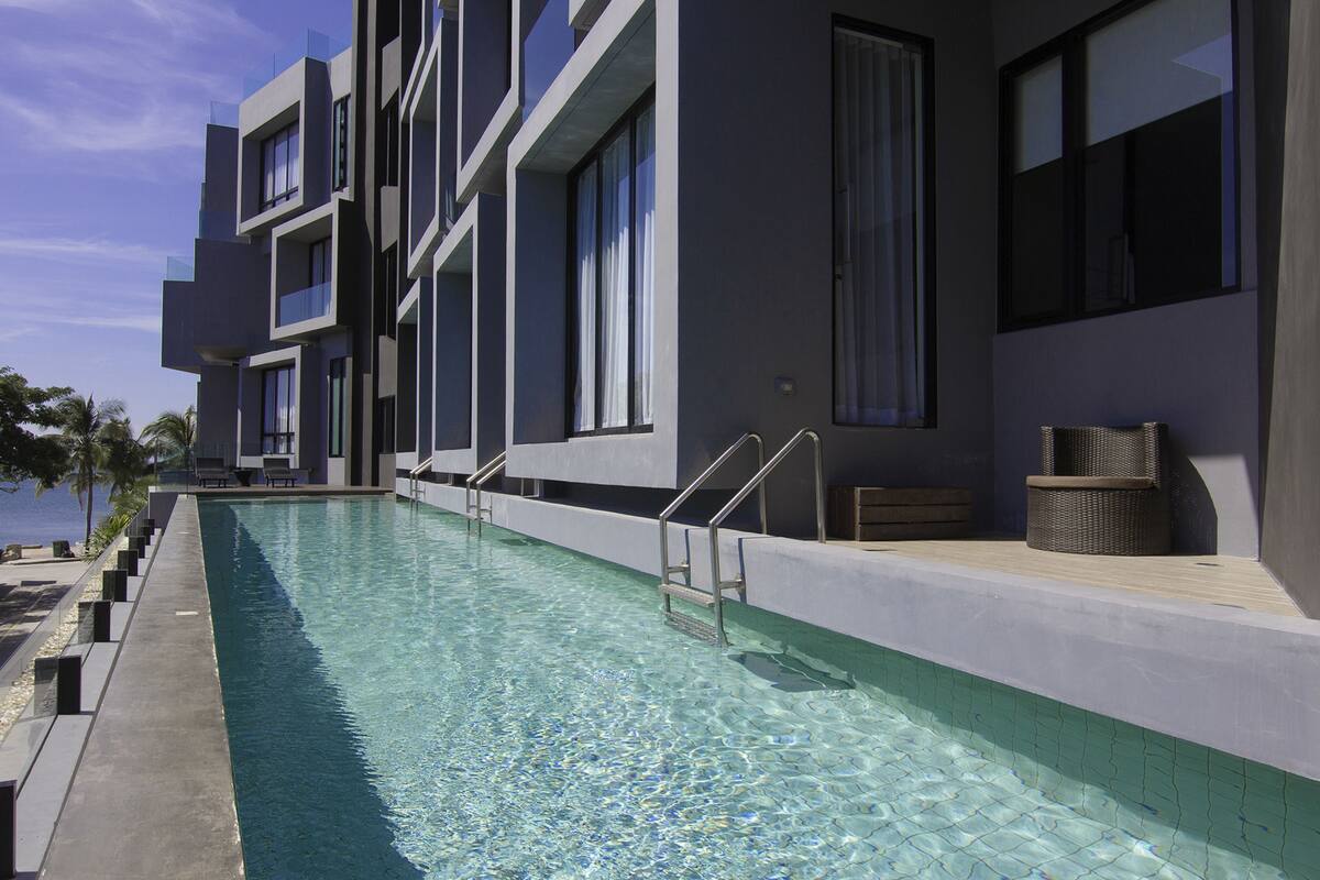 A modern hotel with a swimming pool, outdoor seating, and a view of the sea.