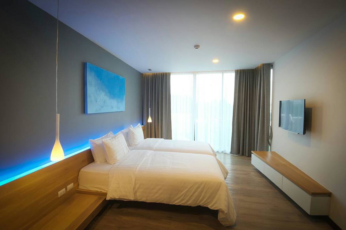 A modern hotel room with two beds, a TV, and a large window with curtains.