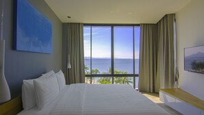 Une chambre d’hôtel avec un grand lit, un tableau au mur, une vue sur l’océan et un téléviseur sur le côté droit.