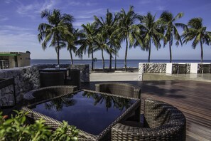 A patio with wicker furniture and a glass table overlooking a beach with palm trees. - Kalm Bangsaen Hotel (Chonburi)