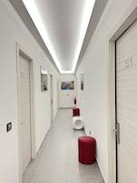 Un pasillo moderno con una larga extensión, puertas numeradas, un extintor y un banco rojo.