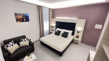A modern hotel room with a large bed, a black sofa, a small round table, and a painting on the wall.