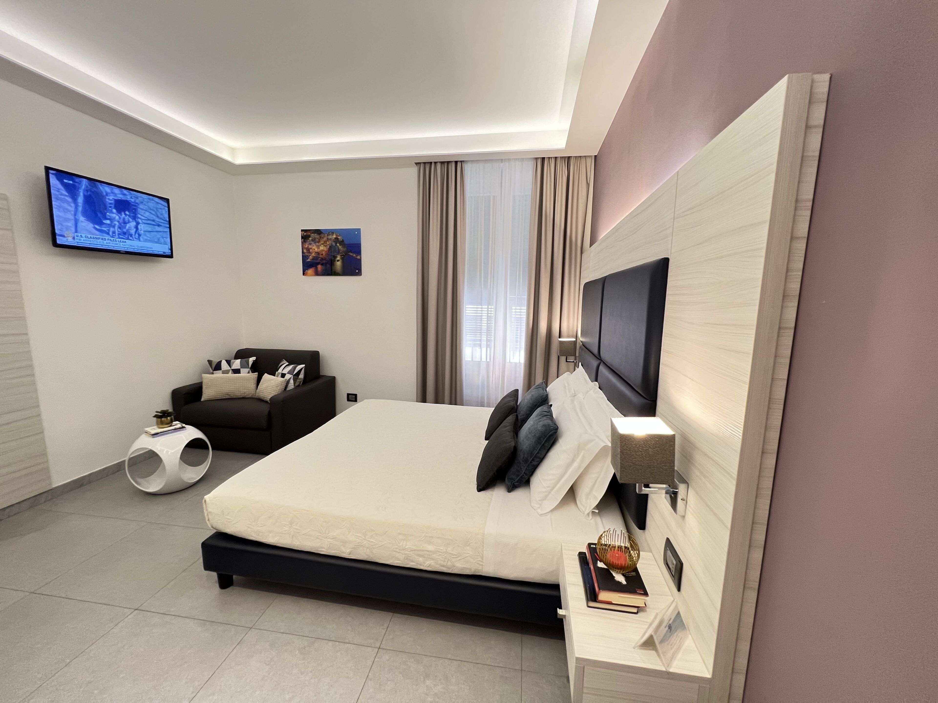 A modern hotel room with a large bed, a flat-screen TV mounted on the wall, a sofa, and a small side table.