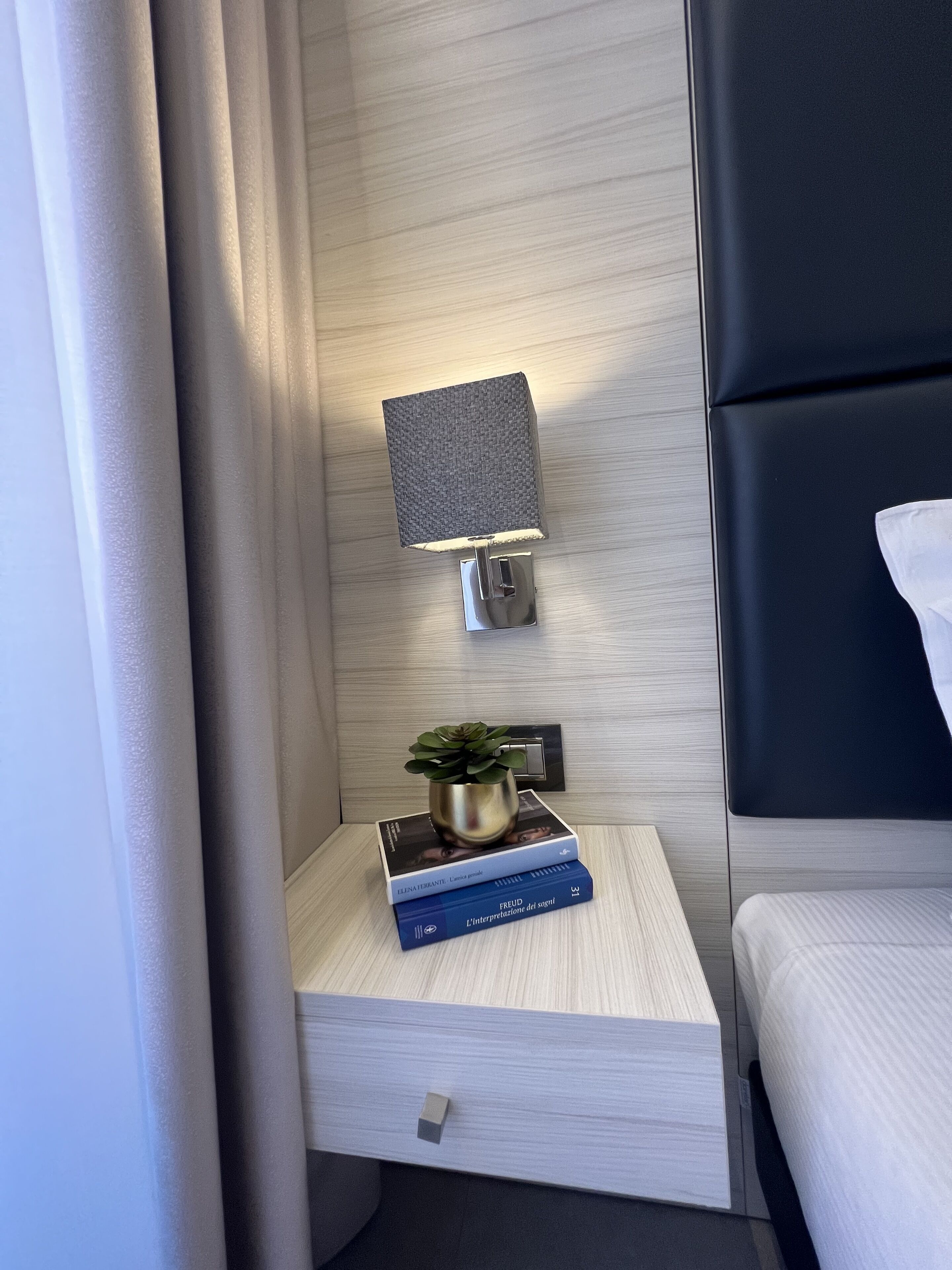 Ein modernes Hotelzimmer mit einem Holznachttisch, einer kleinen Topfpflanze und zwei Büchern.