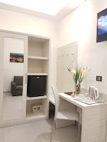 Habitación de hotel compacta con escritorio, silla y un televisor pequeño.