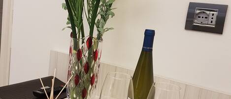 Una mesa con un jarrón de flores, una botella de vino, copas de vino y pétalos de rosa.