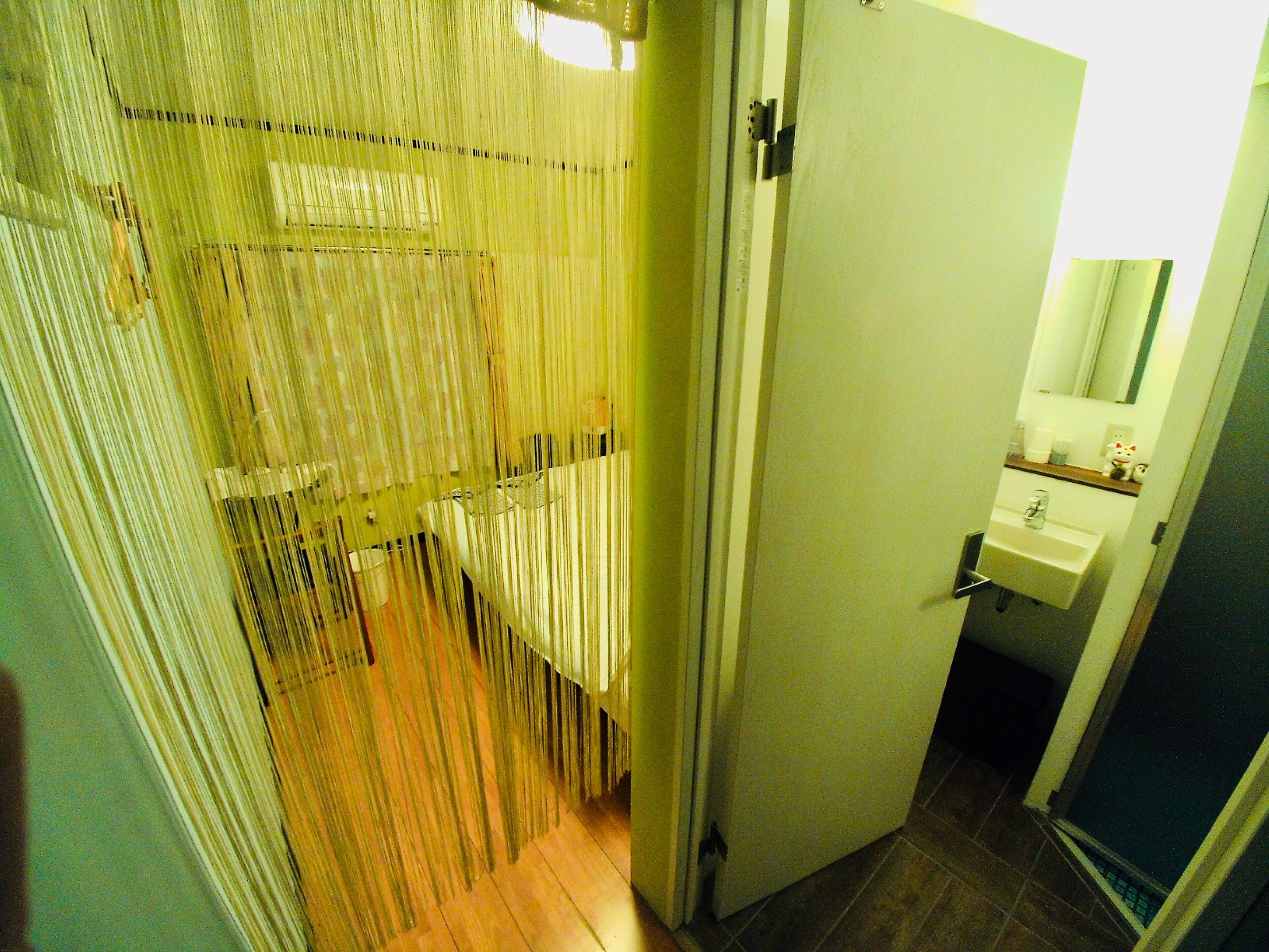 A narrow hallway with a wooden floor, a white door, and a small bathroom with a sink and mirror.