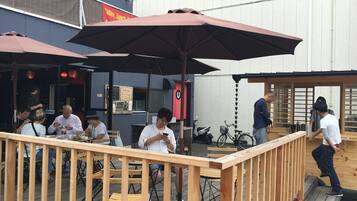 An outdoor seating area with wooden tables and chairs, umbrellas, and a wooden railing.