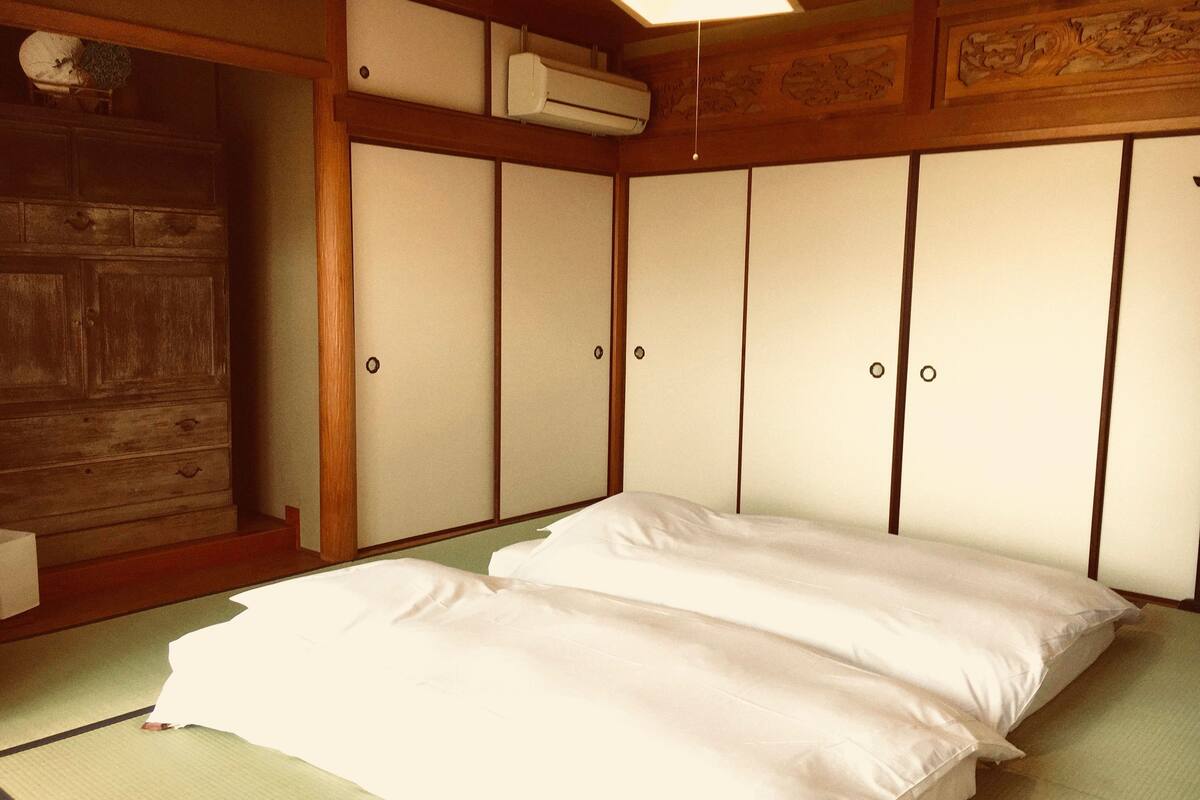 A traditional Japanese-style room with tatami flooring, a futon bed, sliding shoji doors, and a wooden cabinet.