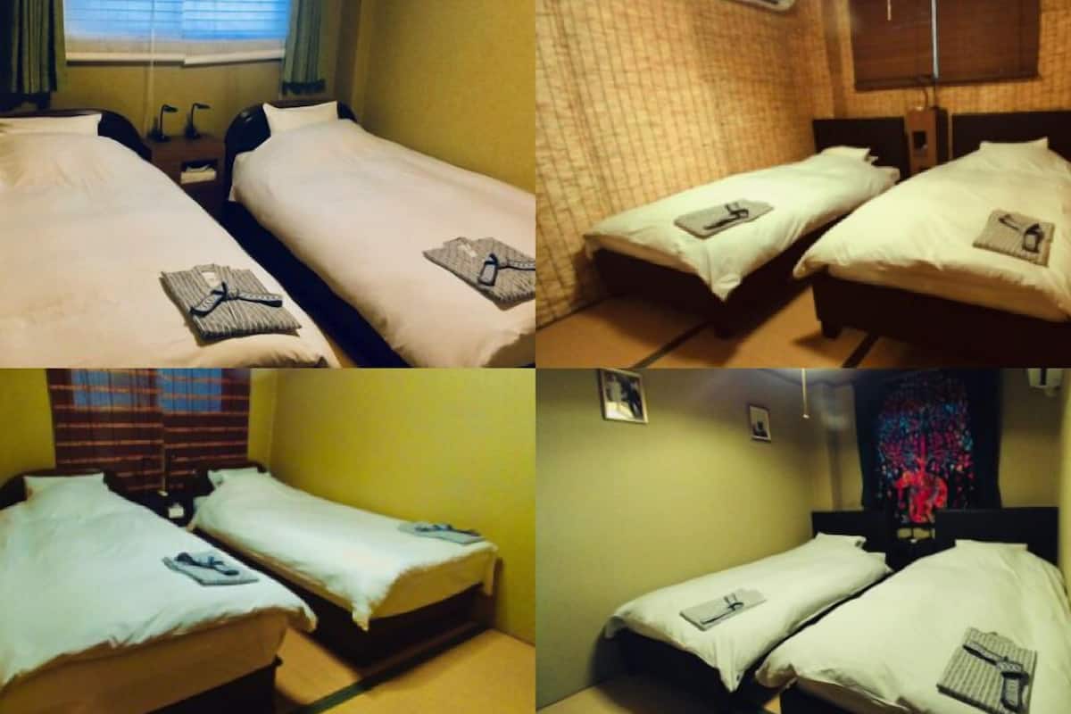 A hotel room with two single beds, a window with curtains, a wall-mounted air conditioner, and a small bedside table with a lamp.