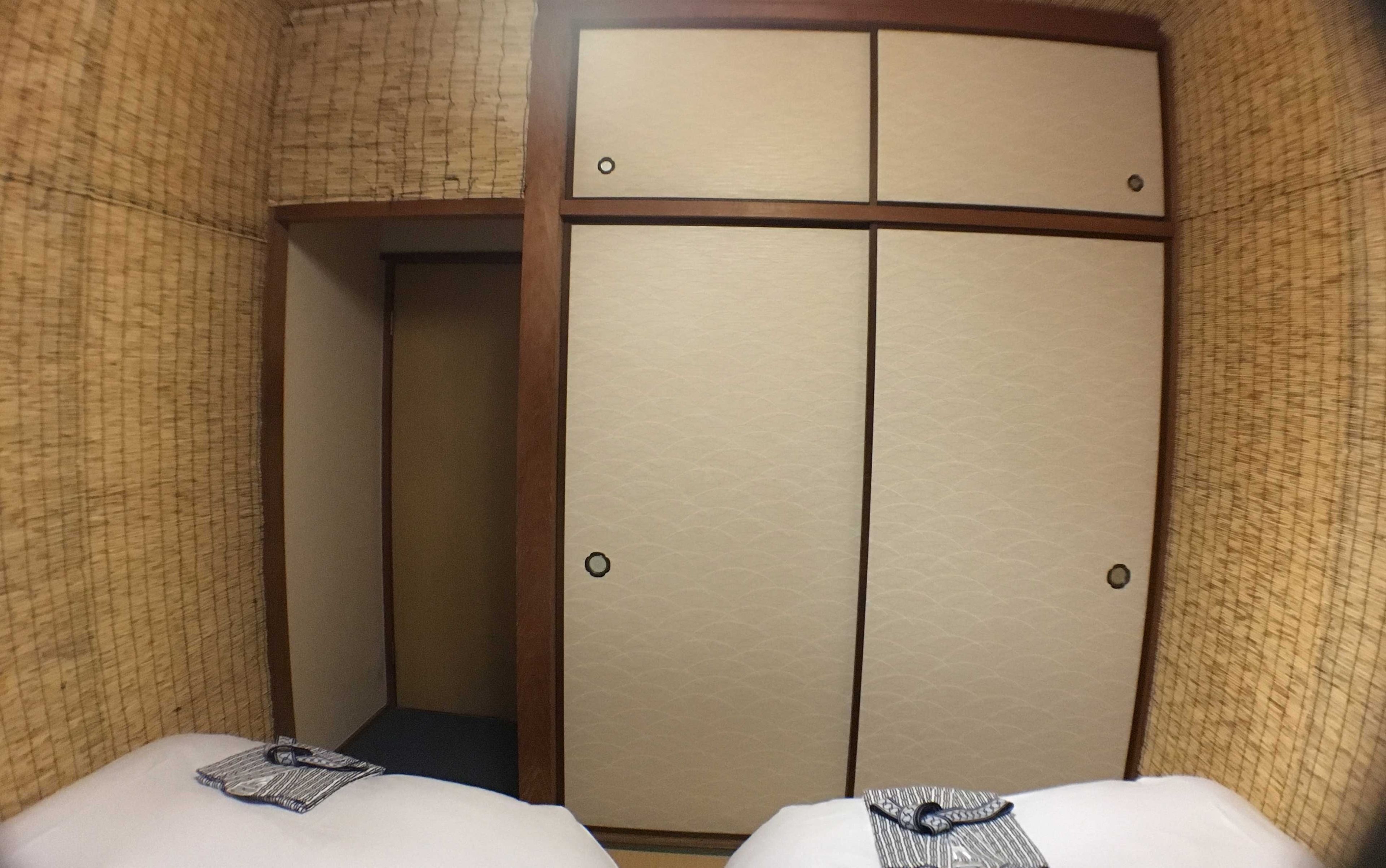 A hotel room with a traditional Japanese-style wardrobe, two beds, and a patterned wall.