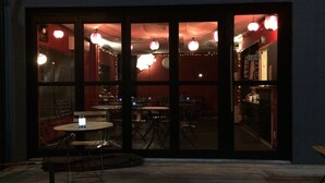 A restaurant with a large glass window, tables, chairs, and string lights. - Uno Port INN (Tamano)
