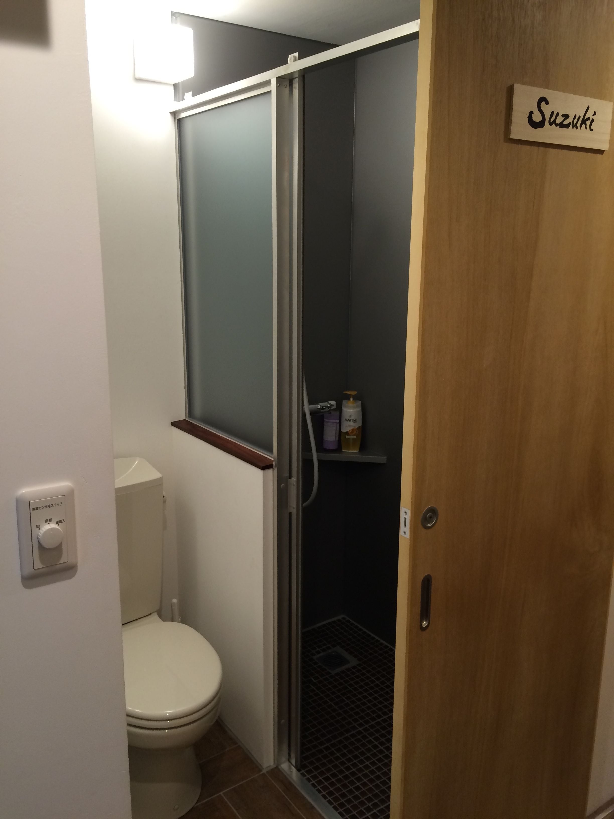 Ein kleines Badezimmer mit Toilette, einer Duschkabine und einer Holztür mit dem Aufschrift 'Suzuki'.