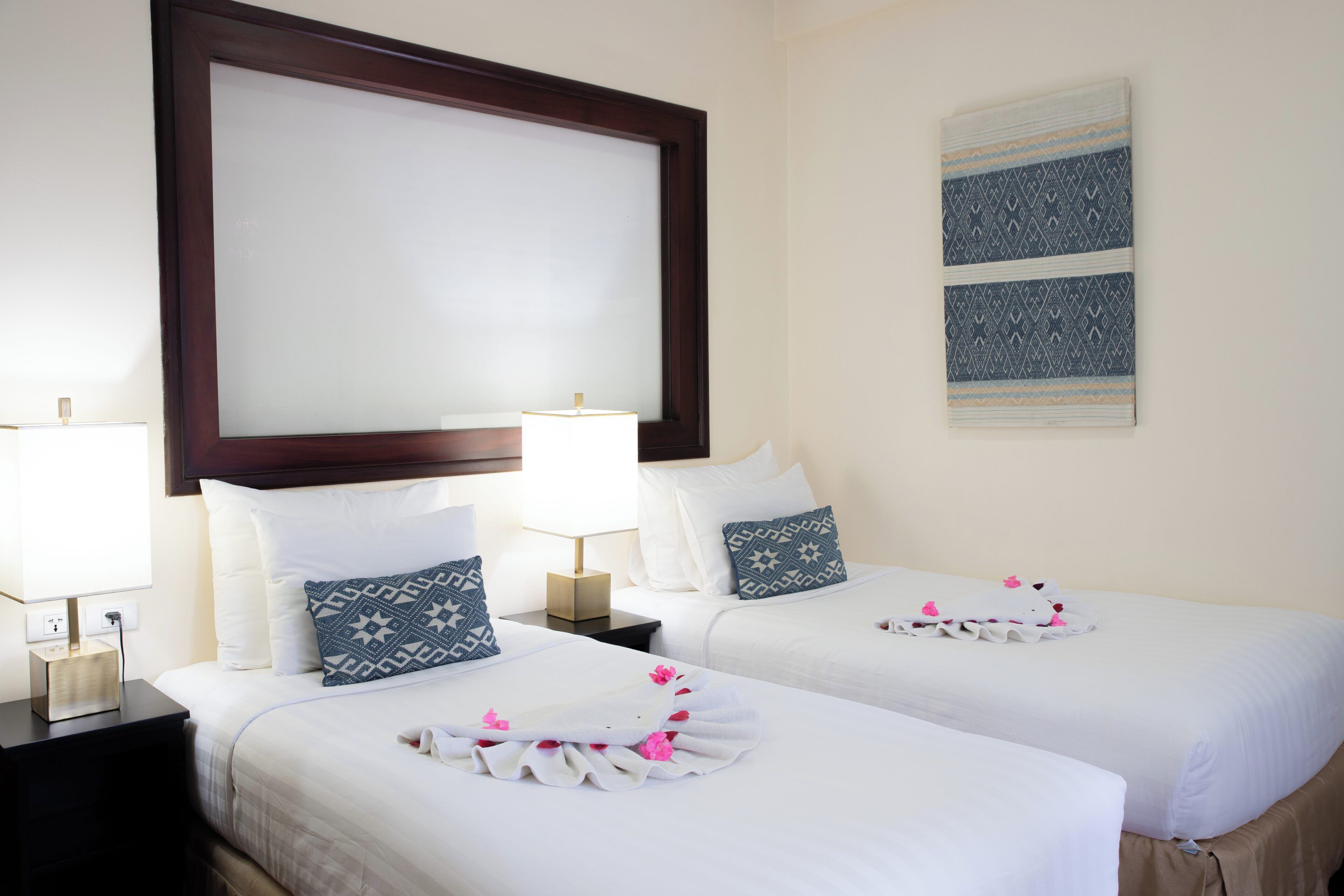 Habitación de hotel con dos camas, un espejo grande, una obra de arte en la pared y una mesita de noche con lámpara.