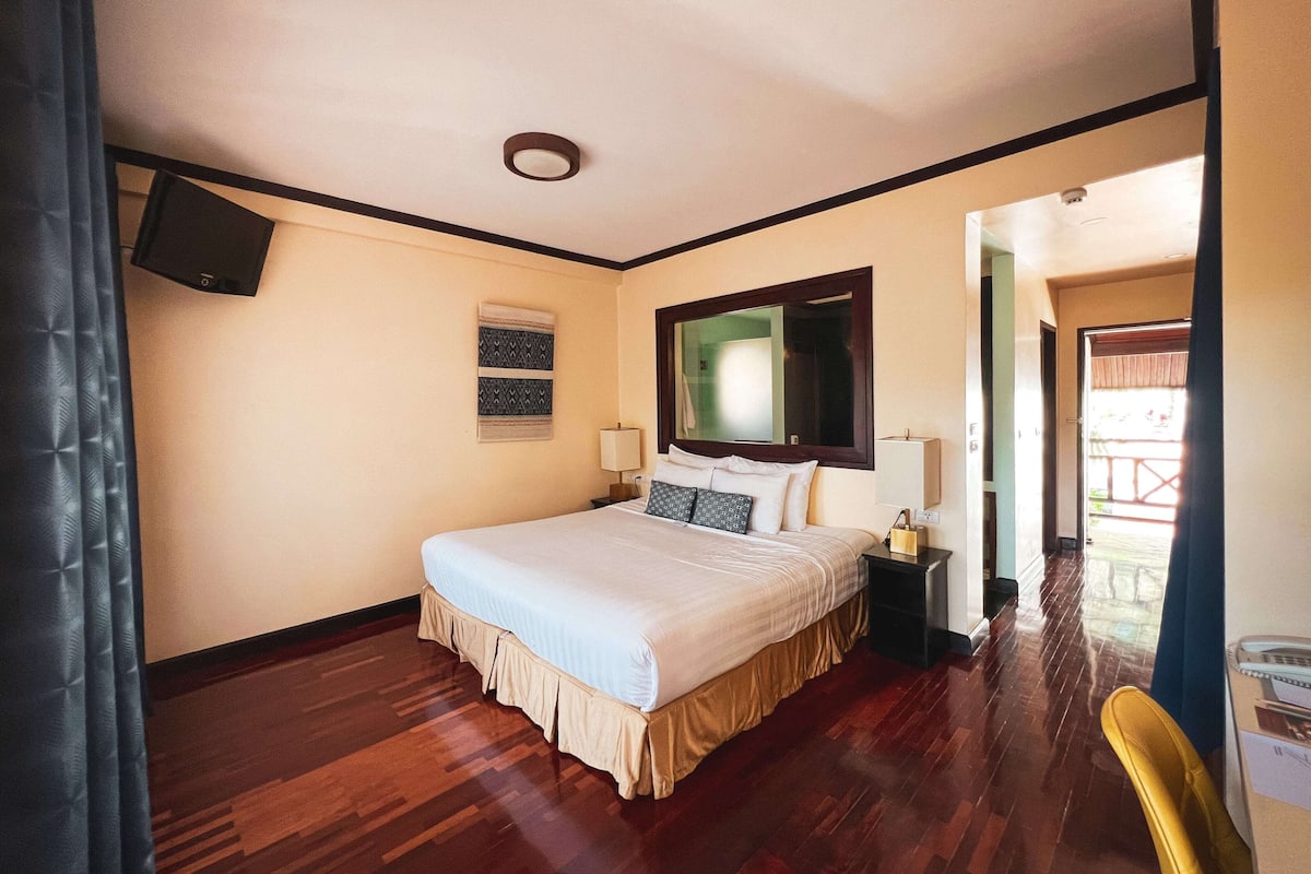 A hotel room with a bed, a flat-screen TV, a mirror, a nightstand, and a door leading to a balcony.