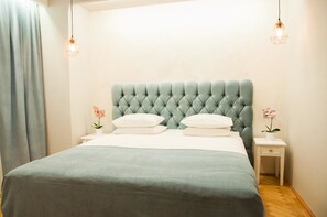A neatly made bed with a tufted headboard, two bedside tables with lamps, and a curtain on the left.