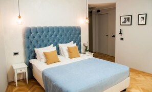 Une chambre à coucher avec une tête de lit capitonnée, du linge de lit blanc et un plancher en bois.