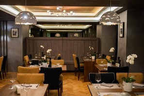Interior de restaurante com várias mesas, cadeiras e luminárias pendentes.