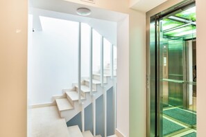 A modern interior with a staircase leading to a second floor, a glass elevator door, and a ceiling with a recessed light fixture.