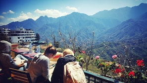 A group of people seated at a table with a mountain view, a water bottle, and a backpack on the table. - Sapa Odyssey Hostel (Sa Pa)