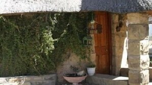 A rustic stone building with a thatched roof, a wooden door, and a potted plant on the ground. - The Green Acorn Guest House (Setsoto)