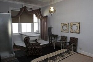 Quarto com banheira, duas cadeiras, uma pequena mesa e detalhes decorativos nas paredes.
